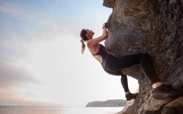 Young female rock climber climbing challenging route on overhanging cliff